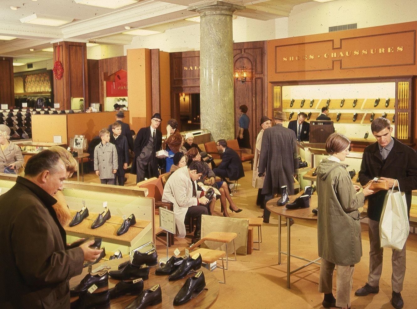 A busy shoe store with customers browsing and trying on shoes at tables and displays.