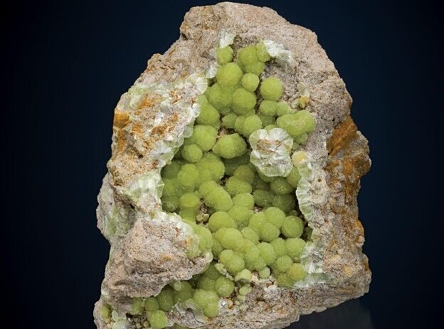 A rough rock with a hollow center filled with green spherical mineral clusters.