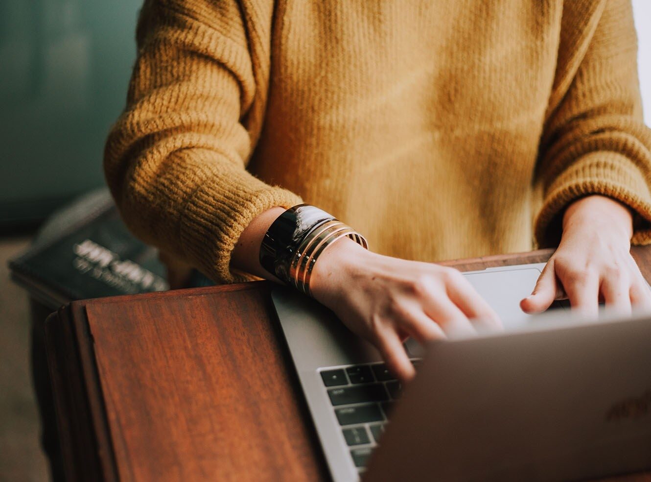 A person wearing a yellow sweater typing on a laptop, with books in the background.