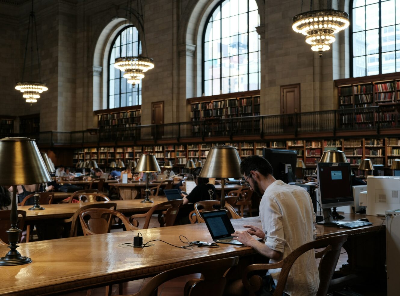 A library interior with tall windows, long wooden tables, and people studying.