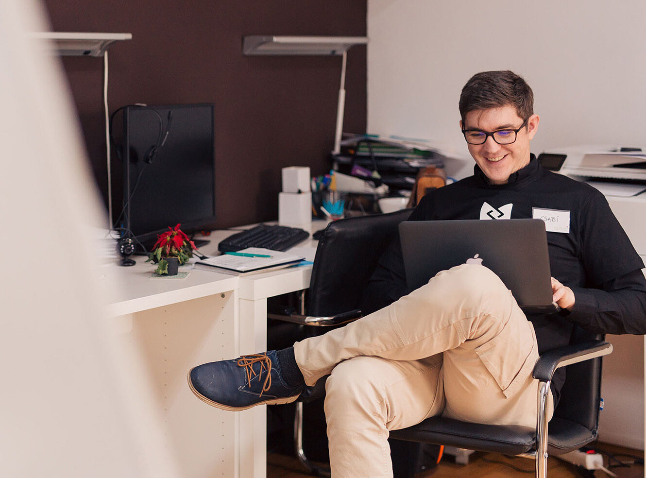A person sitting in a chair, using a laptop with a desk and office supplies in the background
