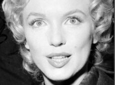 A classic black and white portrait of a woman with curly blonde hair and a bright smile.