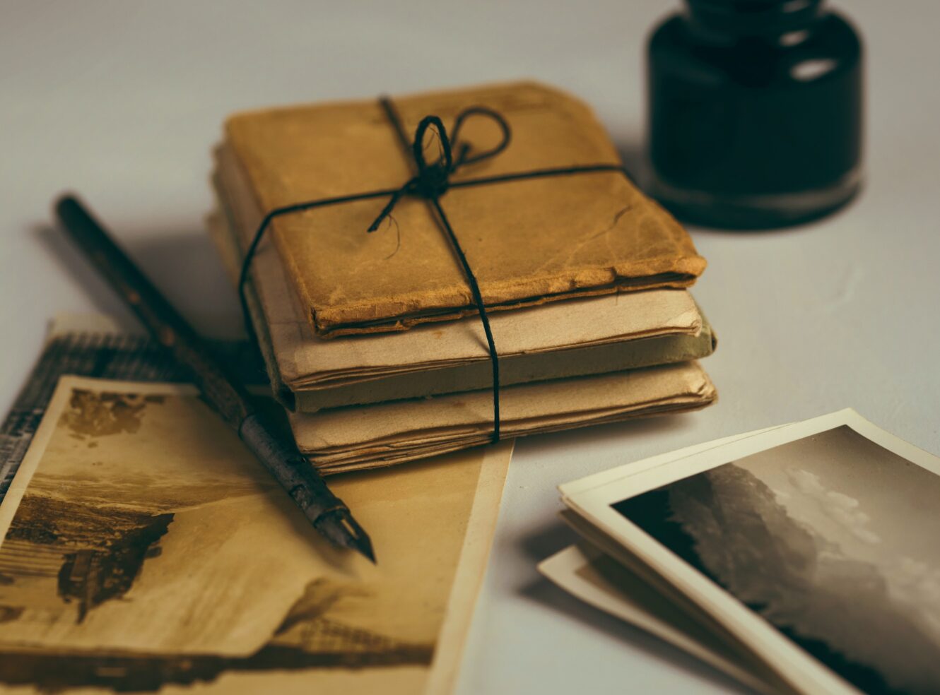 Old stacked envelopes tied with string, a pen, and several vintage photographs