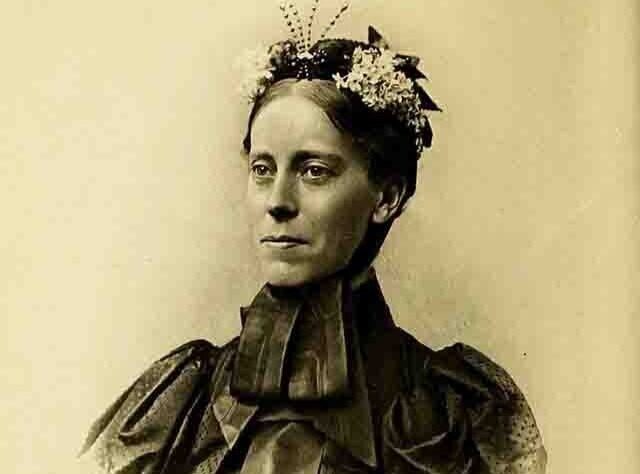 A woman with a flower-adorned headpiece, wearing a dark dress with a high collar.