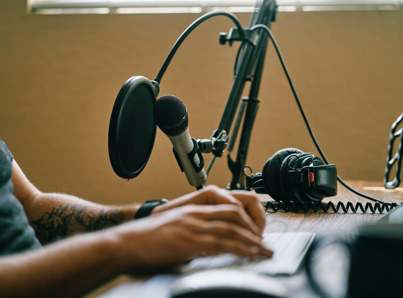 A person with studio recording equipment, microphone and headphones, typing on a keyboard.