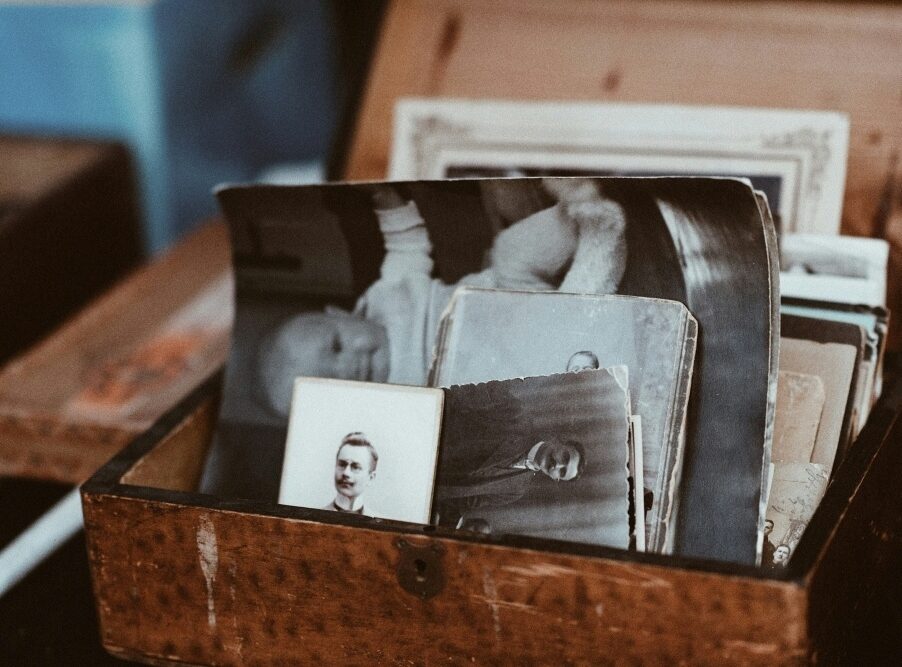 A wooden box filled with assorted old photographs, some in black and white, showing various people.