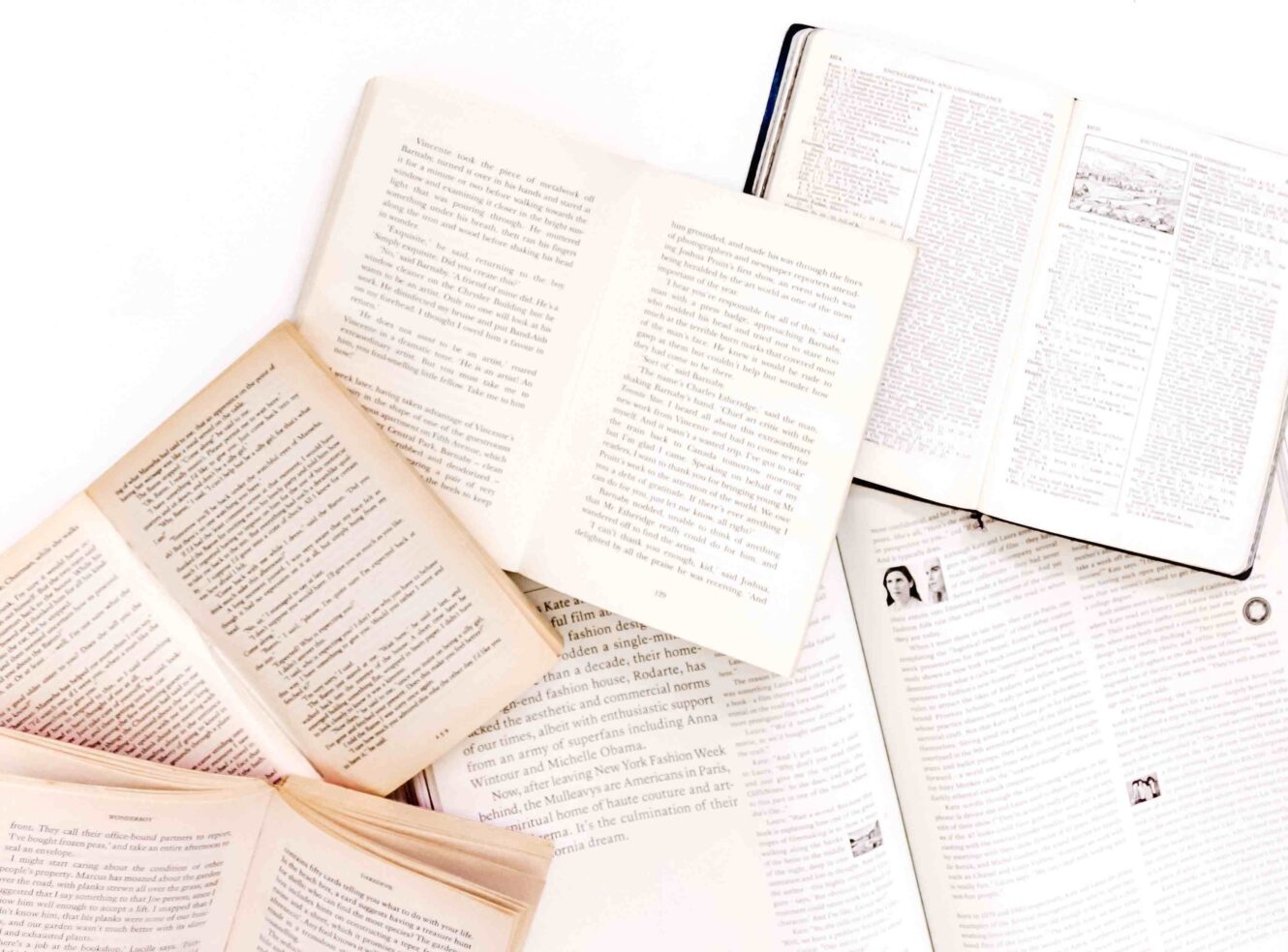 An arrangement of open books with text-filled pages, laid out in a scattered fan-like pattern on a white background