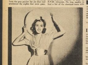 A woman holding a large mirror behind her head, smiling, wearing a light-colored dress.