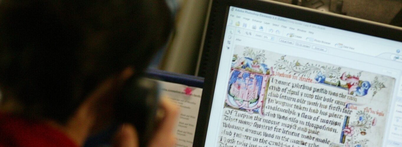 A person sitting at a computer, examining a colourful manuscript on screen.