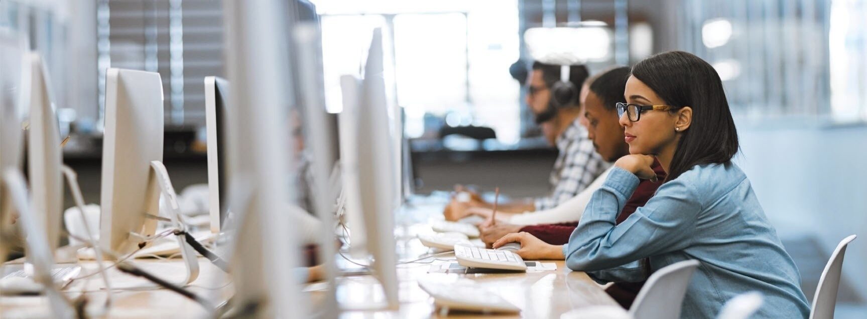 A student wearing headphones, focused on a laptop with a pen in hand.