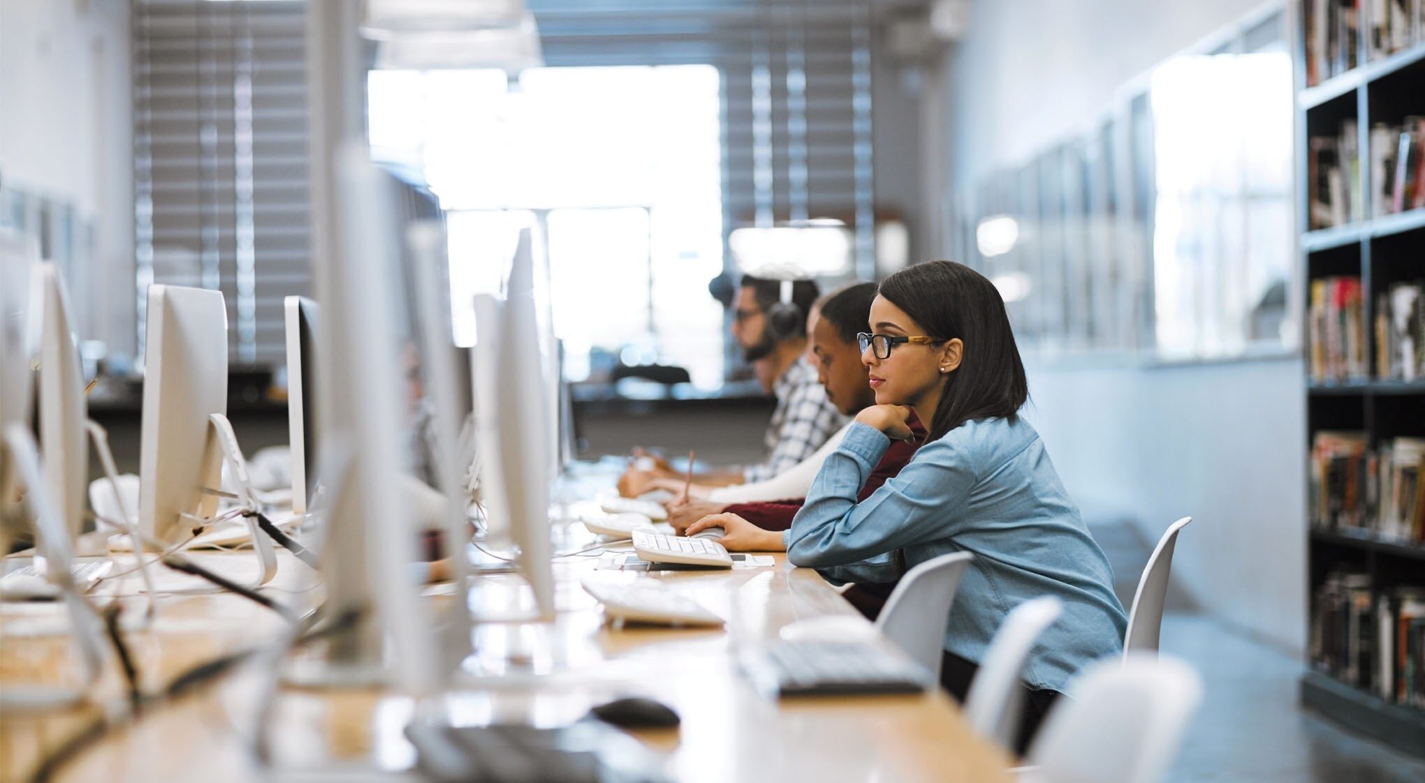 A student wearing headphones, focused on a laptop with a pen in hand.